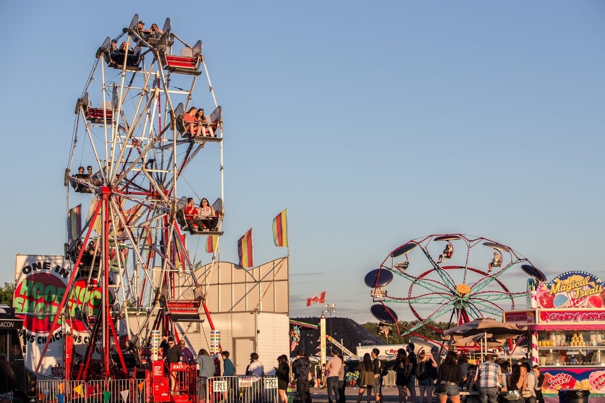 Abendliche Kirmes mit zwei Riesenrädern, beleuchteten Ständen und Besuchern